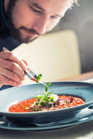 Chef in hotel or restaurant kitchen cooking, only hands. He is working on the micro herb decoration. Preparing tomato soup Chef in hotel or restaurant kitchen cooking, only hands. He is working on the micro herb decoration. Preparing tomato soup.
